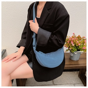 Blue nylon crescent bag with adjustable shoulder strap shown in a stylish outdoor setting