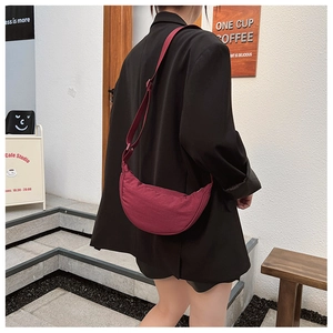 Detailed side view of a burgundy nylon crescent bag with adjustable wide fabric strap