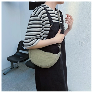 Sage green nylon crescent bag shown on model with striped shirt and black dress