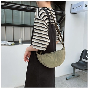 Outdoor shot of grass green nylon crescent bag worn by model over a striped shirt