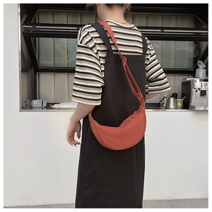 Outdoor shot of an orange half-moon crossbody bag shown on model for size and fit