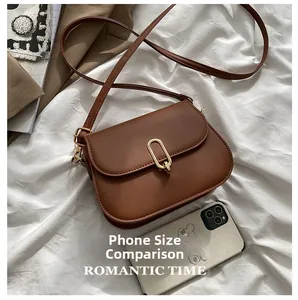 Detail view of brown leather saddle bag with gold buckle next to a phone for size reference
