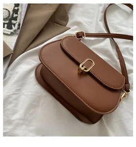 Detailed close-up of brown leather crossbody bag with elegant gold metal clasp on fabric