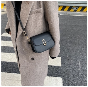 Close-up of black crossbody bag with gold U-shaped buckle on dark grey coat