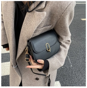 Close-up of black crossbody bag with gold metal lock on woman in wool coat