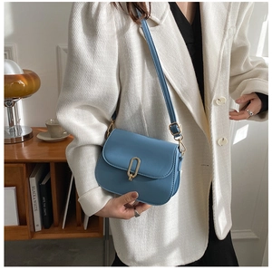 Detail of misty blue leather crossbody bag with a signature oval gold metal buckle