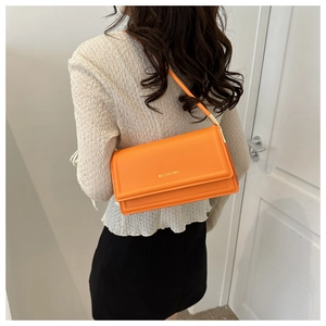 Detail van een oranje minimalistische crossbody tas met gouden logo en gladde textuur