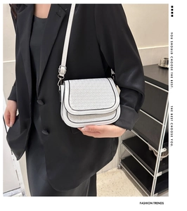 Close-up of white woven saddle bag with black piping and embossed patterns on shoulder strap