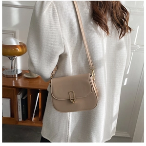 Close-up of beige saddle bag with oval gold buckle and strap worn on the shoulder