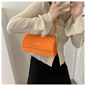 Detail van oranje kunstleren handtas met geometrische reliëflijnen en gouden logo