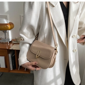 Detail of a beige crossbody square bag with a golden U-shaped buckle on a white blazer