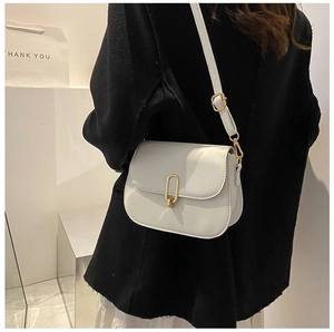 Detail view of a white leather crossbody bag with a gold oval metal clasp worn by a model