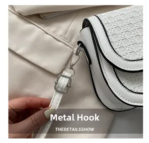 Detail of silver hardware hook and woven texture on white saddle bag with black trim