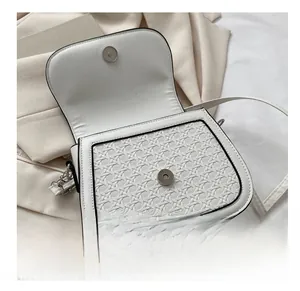 Detail view of woven texture white saddle bag with black trim and magnetic hardware closure