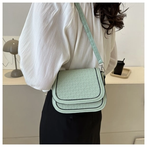 Close-up of mint green woven texture and black piping on stylish faux leather saddle bag