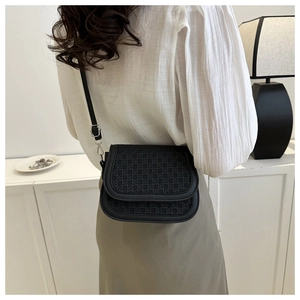 Detail of a black woven saddle bag with adjustable shoulder strap and silver hardware