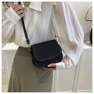Close-up of a black crossbody bag featuring a woven texture flap and leather strap