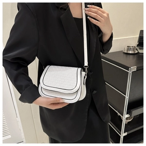 Detailed view of a white woven saddle bag with black trim on a model in a black suit