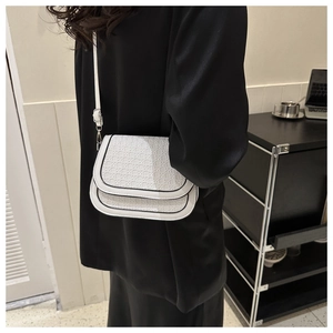 Close-up of a white woven saddle bag with black trim and silver hardware on a model