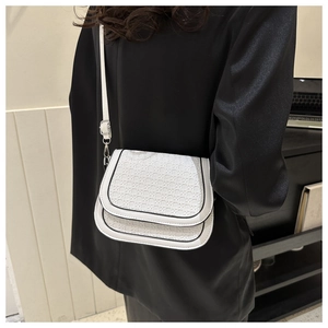 Detail of white woven texture saddle bag with black contrast piping and adjustable strap