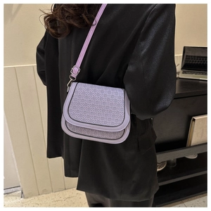 Detail of lavender woven crossbody saddle bag worn on a black textured blazer