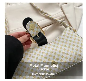 Détail du fermoir magnétique doré sur le sac à bandoulière blanc à motifs monogramme