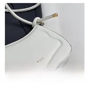 Detail der cremeweißen Satteltasche aus Leder mit goldenen Beschlägen und feiner Naht
