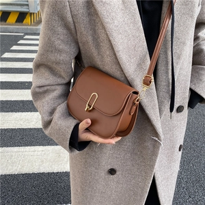 Brown leather saddle bag with gold U-lock worn with a grey wool coat in street style