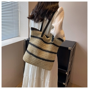 Rear view of model wearing a woven straw tote bag with black stripes and long shoulder straps