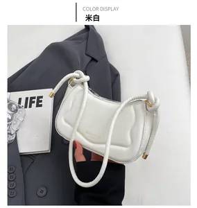 Detail der cremeweißen gesteppten Satteltasche auf grauem Blazer mit Golddekor