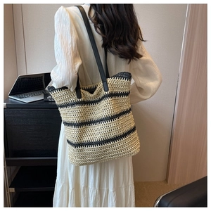 Detail of hand-woven straw tote bag with black contrast stripes and faux leather strap