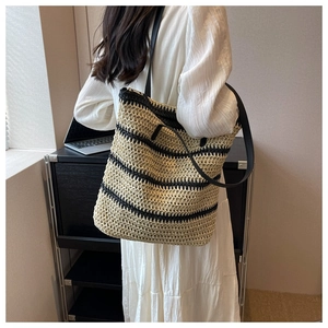Detail of woven straw tote bag with black stripes and leather shoulder strap on a model