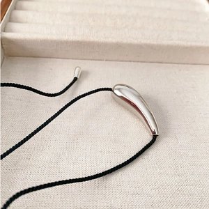 Minimalist silver teardrop pendant necklace with black cord on cream jewelry box
