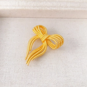 Broche nœud élégante dorée avec texture perlée pour pulls et manteaux sur tissu