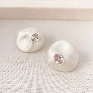 Macro view of irregular pearl-white stud earrings with sparkling center zircon detail