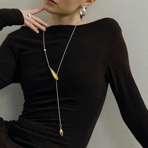Lange Y-Halskette mit goldenem Blattanhänger und Perle auf dunkler Strickmode