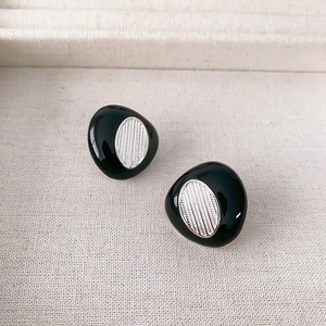 Irregular black enamel pebble earrings with textured silver center on white fabric