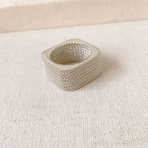 Modern square silver metal ring with textured mesh finish on a rustic fabric background