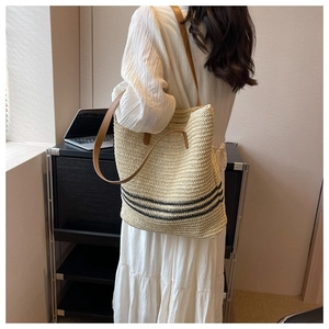 Detail of woven straw tote bag with black stripes and brown leather strap on model