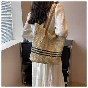 Detail of woven straw tote bag with black stripes and brown leather handles on shoulder