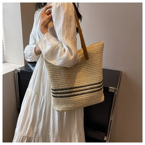 Model wearing a large woven straw tote bag with black stripes and brown leather straps