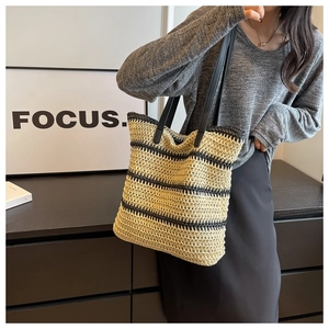 Detail of hand-woven striped straw tote bag with black leather handles carried by a model