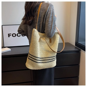 Detail of woven straw tote bag with black stripes and brown leather shoulder straps