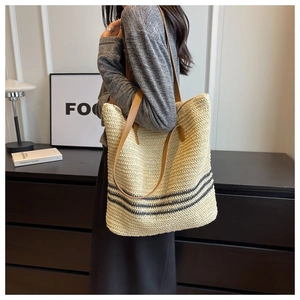Close-up of woven straw tote bag with black stripes and brown faux leather straps