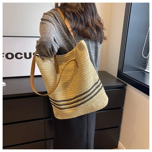 Close-up of woven tote bag with retro black stripes and brown leather straps worn by model