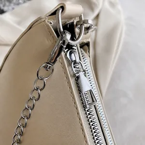 Detailed macro shot of smooth silver zipper and chain hardware on a beige leather bag