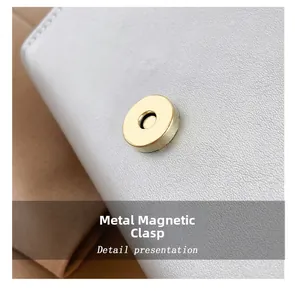 Detail of golden magnetic buckle on white pebble leather bag with fine stitching