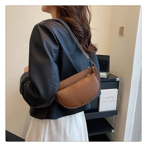 Detail of a brown leather saddle bag with silver chain strap worn by a female model