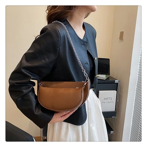 Detail of brown half-moon saddle bag with metal chain strap and layered zipper design