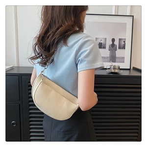 Detail of a beige saddle bag with silver chain strap and matte synthetic leather texture